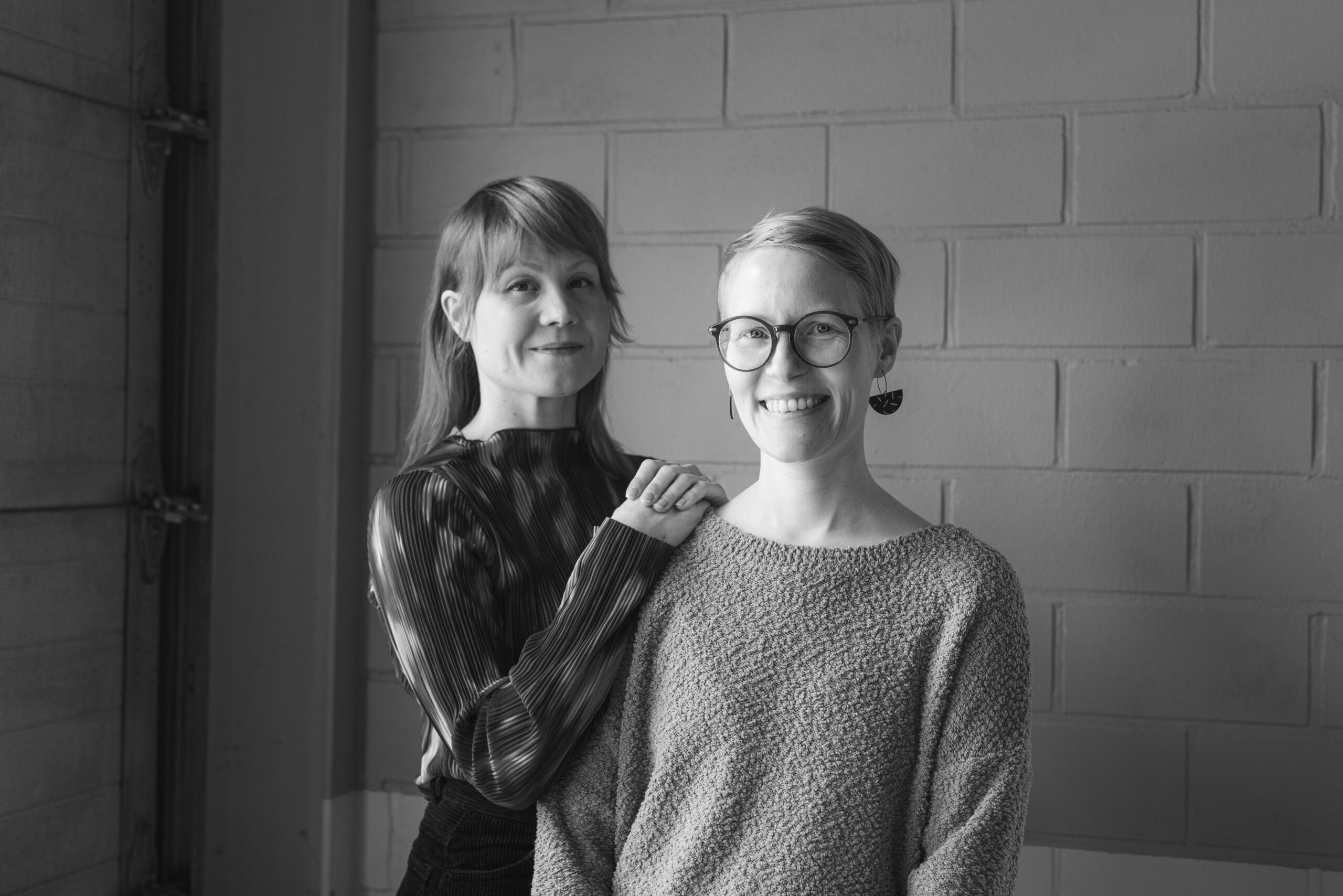 Elisa Itkonen ja Suvi Koivisto hymyilevät ja katsovat kohti kameraa. Itkonen nojaa käsillään Koiviston olkapäähän.