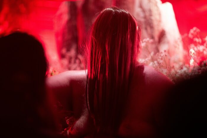 A person sitting, long hair covering the face, in a red light.