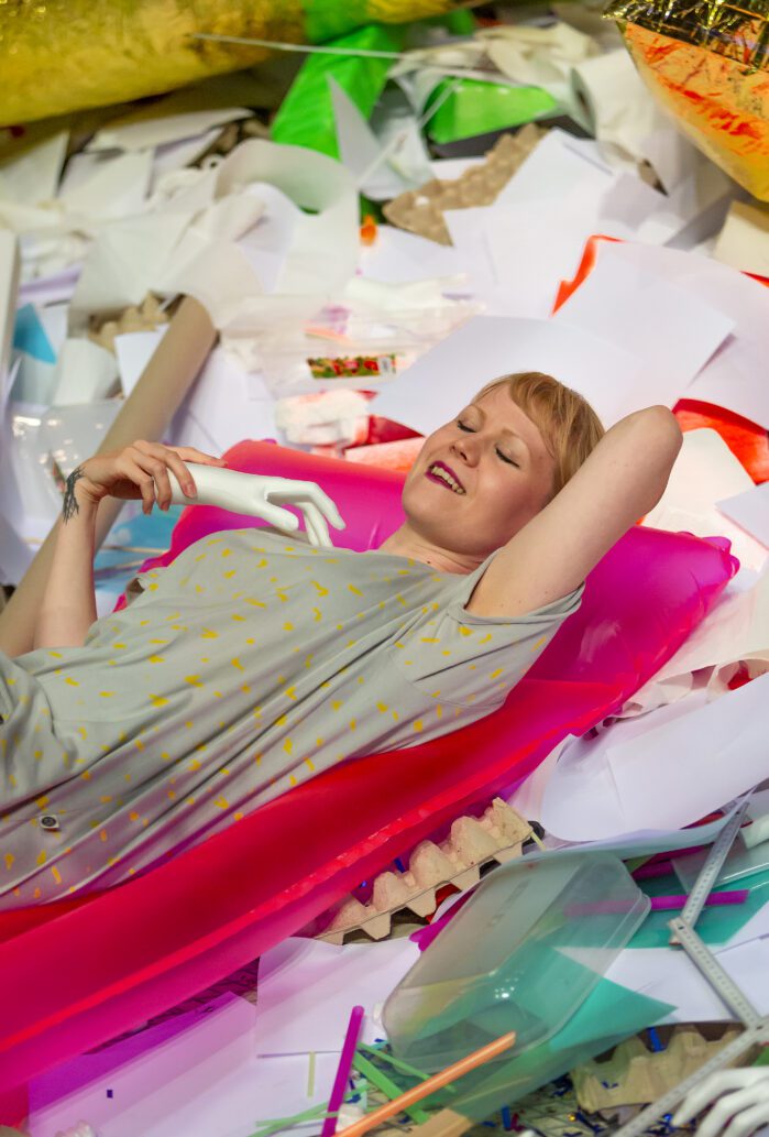 Elisa Itkonen smiling and resting on a pink mattress, in the middle of a live performance.