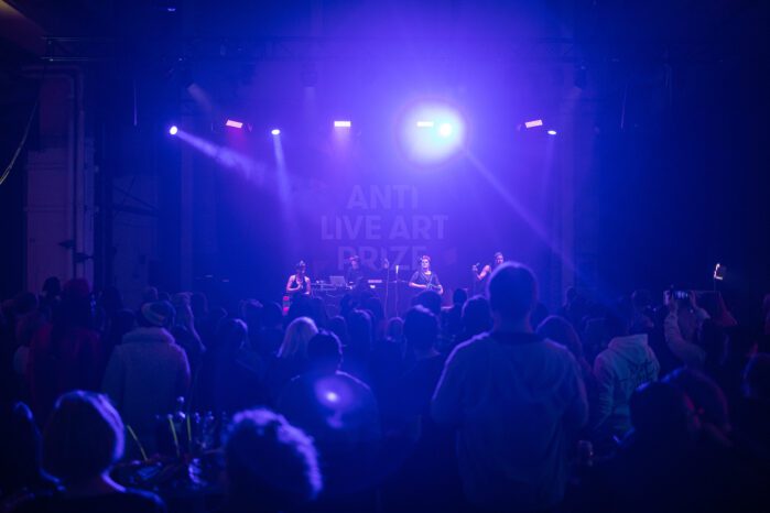 A crowd in a large room, blue lightning, a band playing at a stage in front of people.