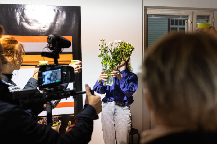 Elisa Itkonen ojentaa kukkakimppua kohti videokameraa, joka etualalla.