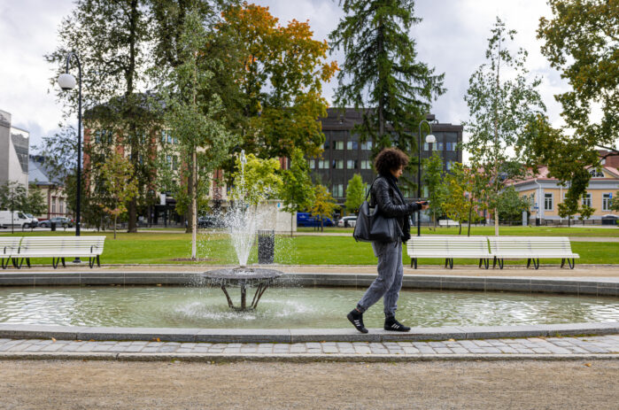 A person walking in front of a fountain in a park.