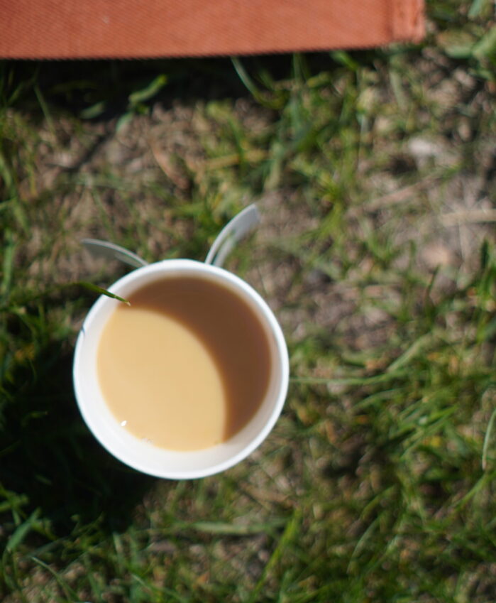 A cup of coffee outside in the ground.