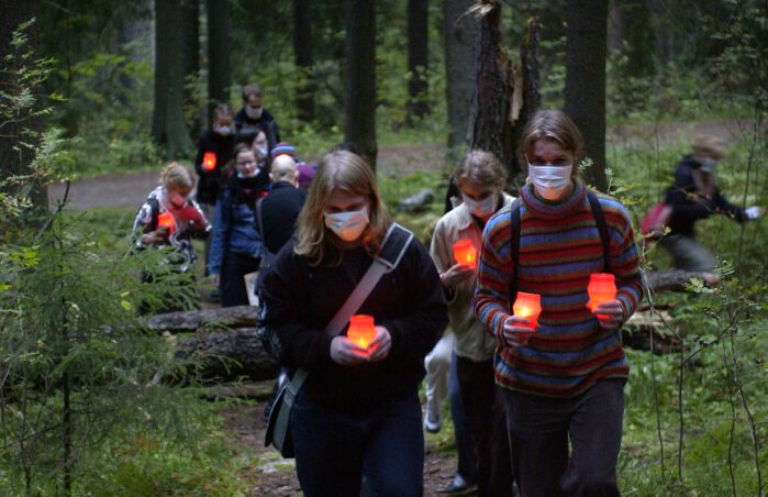 Joukko ihmisiä kantaa kynttilöitä metsässä.