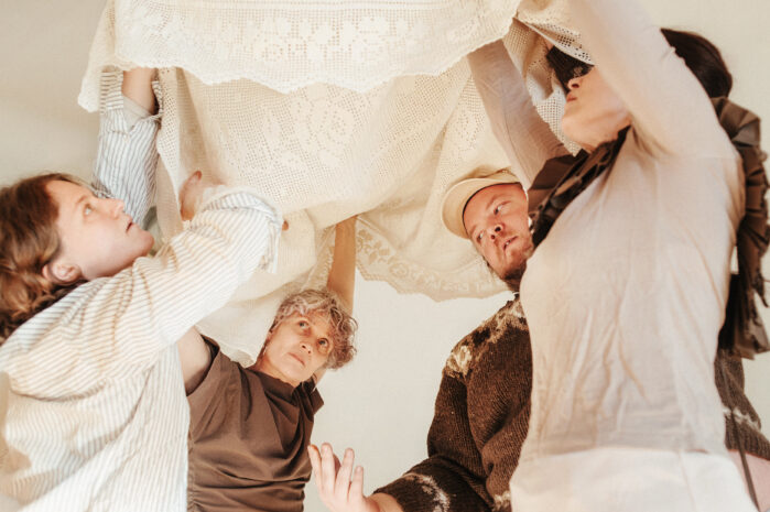 Four performers are holding a white cloth with their hands above their heads.